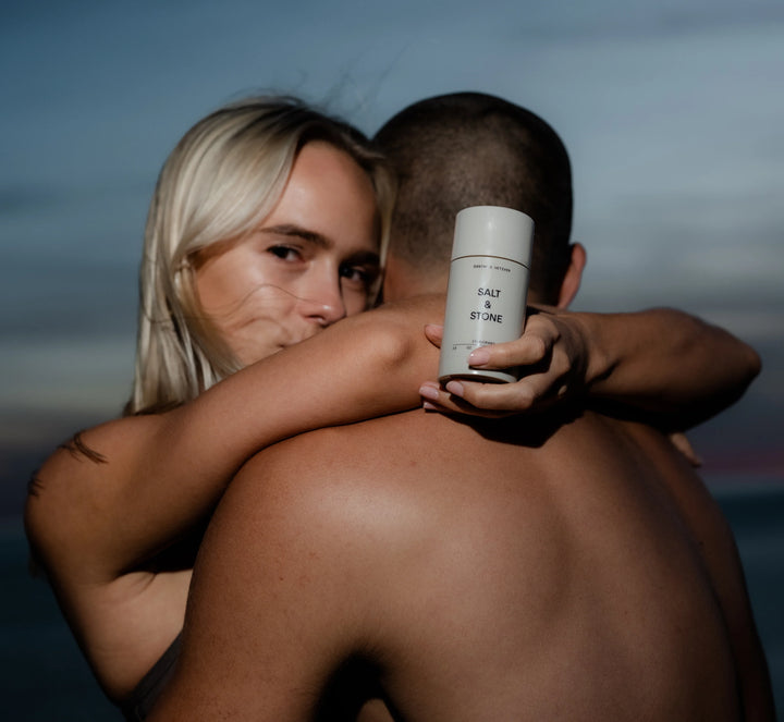 Two people holding Salt and Stone deodorant at the beach